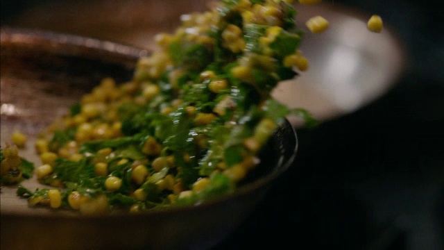 在餐厅的厨房里，厨师用慢动作在燃烧的火炉上用铁煎锅翻炒玉米煮玉米视频素材
