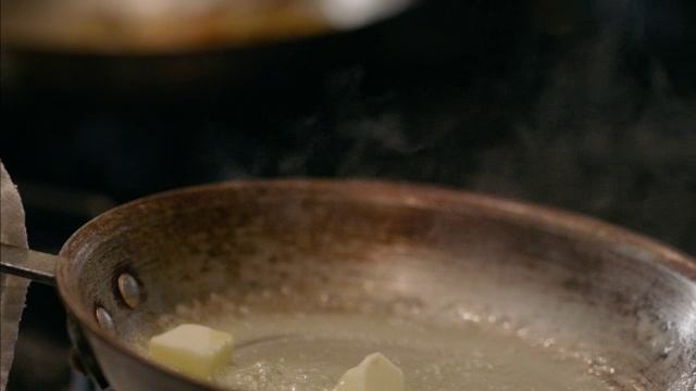 在餐厅的厨房里，厨师用慢动作将融化的黄油放在热气腾腾的煎锅周围视频下载