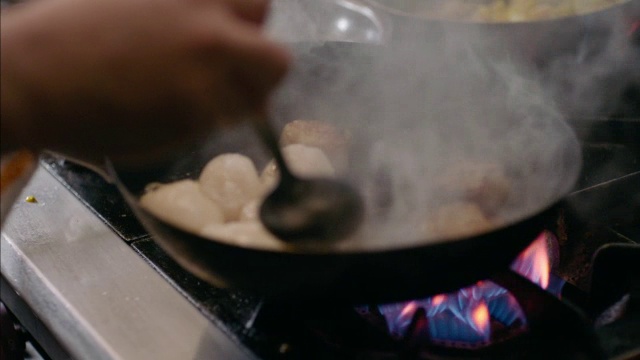 在餐厅的厨房里，美食厨师用慢动作把扇贝放在平底锅上，放在燃烧的煤气炉上视频素材
