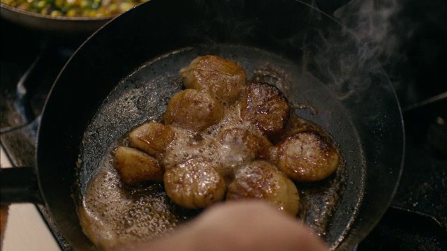在餐厅厨房里，厨师用慢动作在铁锅里滋滋作响的扇贝上洒油视频素材
