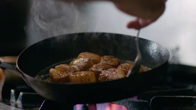在餐厅的厨房里，厨师在铁锅里慢动作地把油抹在滋滋作响的扇贝上视频下载