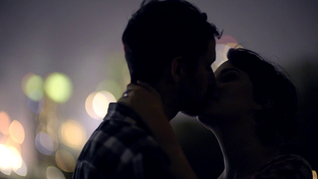 年轻的情侣亲吻着城市的天际线，远处的烟花照亮了夜晚视频素材