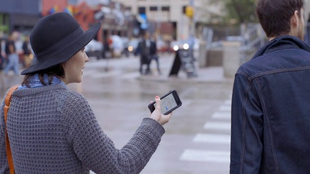 一对迷路的年轻夫妇在奥斯丁市中心闲逛，在人行横道前停下，在智能手机上看路视频下载