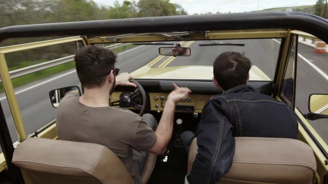 两个年轻人开着经典的福特野马在乡村崎岖的道路上奔驰视频素材