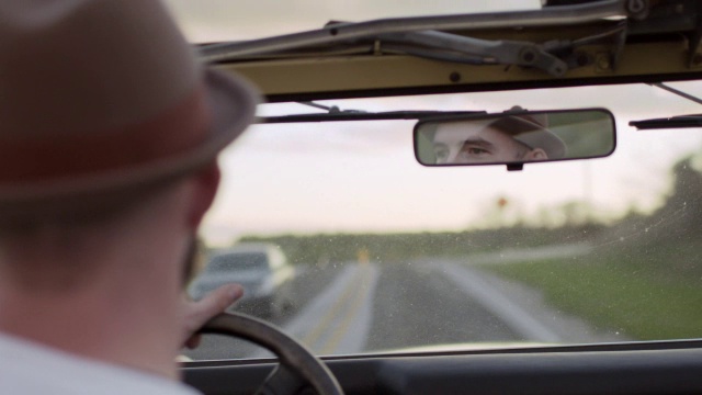 一个年轻人开着老爷车在乡间小路上行驶，从后视镜里可以看到他的眼睛视频素材