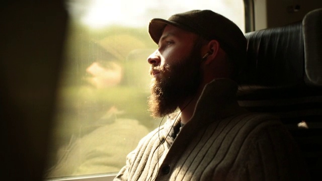 近距离观察一个戴着耳机的年轻人看着窗外行驶的火车视频下载