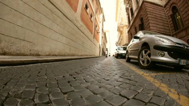 手持式低角度广角拍摄意大利男子驾驶摩托车在小巷在罗马，意大利。视频下载