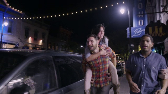一个年轻的女人骑在一个男人的背上，他们在德克萨斯州的奥斯汀市中心散步视频素材