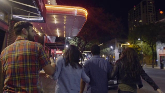 朋友们手挽手走过奥斯汀市中心，在闪烁的电影院大屏幕下视频下载