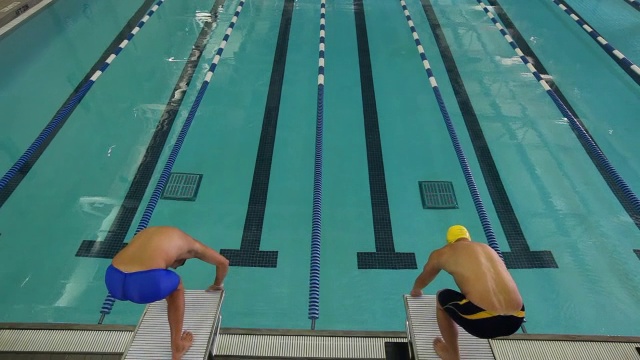 游泳者走上一个平台，摆出出发姿势，然后向前跳水。视频素材