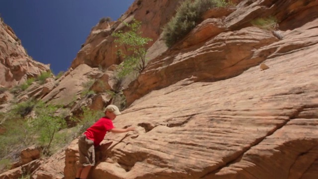 从阳光和岩石峡谷壁倾斜下来，展示了年轻的徒步男孩攀登峡谷的一侧视频素材