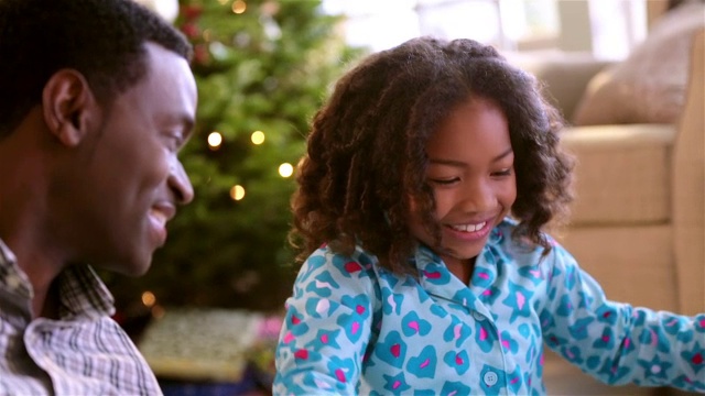 可爱的小女孩微笑的父亲，当她解开礼物在圣诞节的早晨视频下载