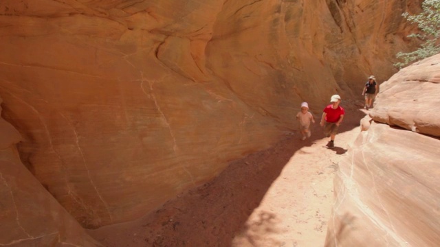 年轻的徒步旅行者男孩和年轻的徒步旅行者女孩和他们的母亲跑下一条小径在一个狭窄的红色摇晃的峡谷视频素材