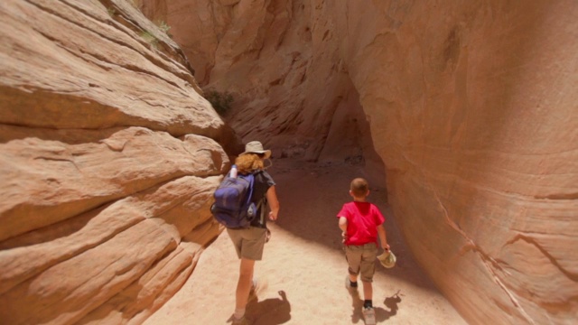 母亲和她年幼的儿子走过一条狭窄的红色摇晃的峡谷，环顾四周视频素材