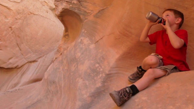 小男孩喝着水瓶，躺在红色的峡谷壁上休息视频素材
