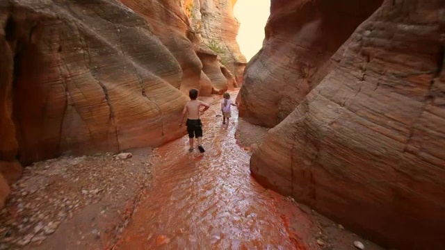 跟随年轻的徒步旅行者男孩和年轻的徒步旅行者女孩下河床通过峡谷狭窄视频下载