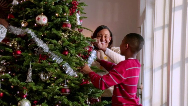 小男孩帮助爸爸妈妈在圣诞树上挂金箔视频素材