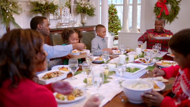 家人在桌子周围传递圣诞晚餐的盘子，可爱的小女孩闻着饥饿的红薯，父亲为他们服务(多莉镜头)视频素材