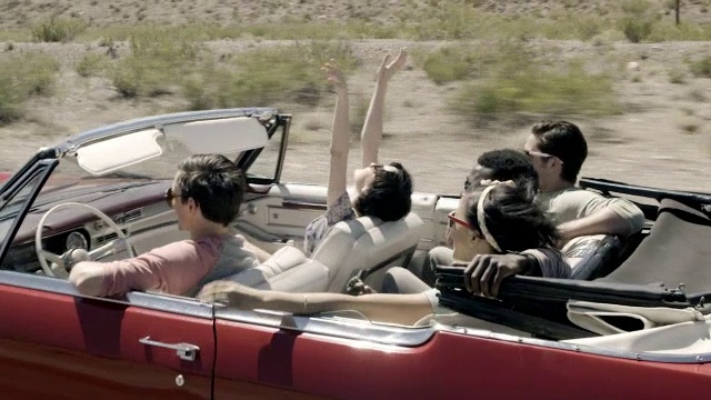 一群朋友开着红色的敞篷车穿过沙漠，女孩们把手举在空中视频素材