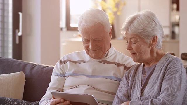 一对老年夫妇微笑着看数字平板电脑上的东西视频素材