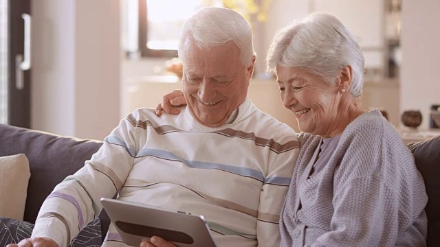 一对老夫妇一边看数字平板电脑一边笑视频素材