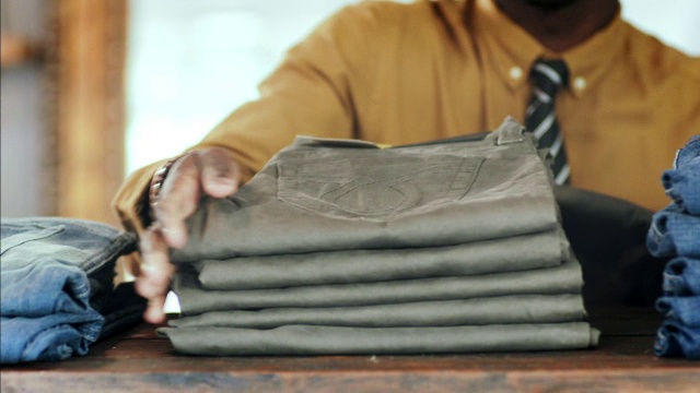 年轻的员工在当地服装店的货架上堆放折叠的裤子视频下载