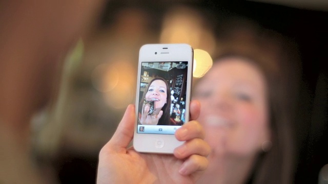 一个年轻的女人飞吻，她的男友用手机拍下了她的照片。视频素材