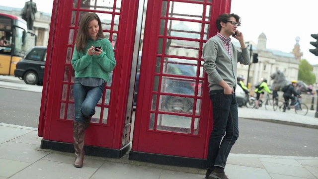 年轻人在电话亭附近打手机。视频素材