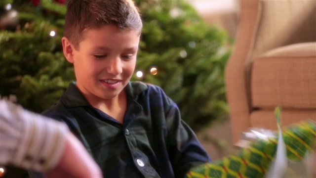 一个小男孩疯狂地撕下包装纸，在圣诞树前打开礼物视频下载