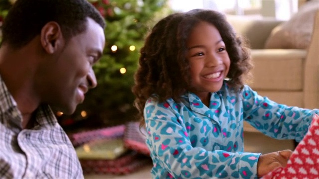 可爱的小女孩微笑着看着爸爸，泪水被包装纸在圣诞节的早晨视频下载