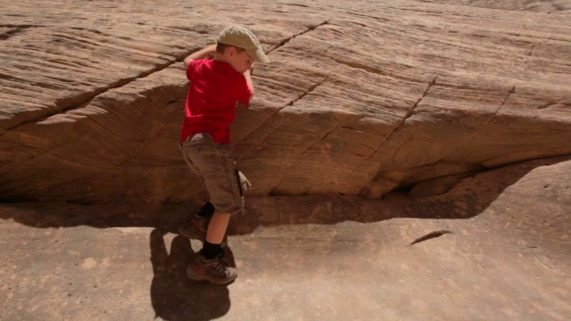 镜头跟随一个年轻的徒步男孩爬上岩石峡谷壁视频素材