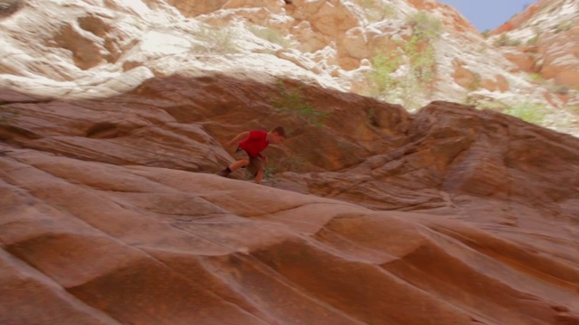 年轻的徒步旅行者走下陡峭的红色的峡谷岩壁视频素材