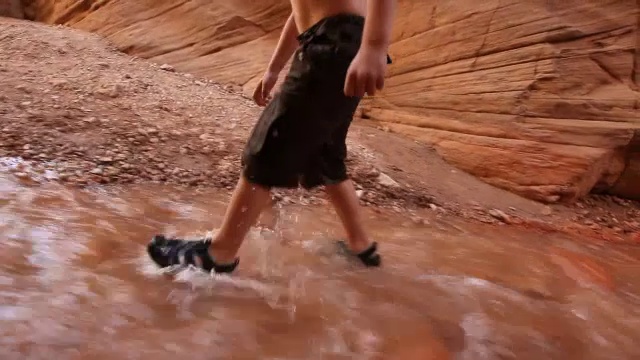 小徒步男孩的河鞋的特写，因为他徒步通过峡谷河床视频素材