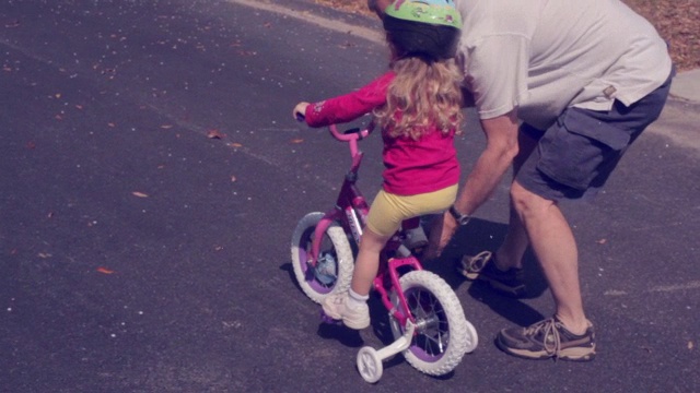 一个爷爷教一个小女孩第一次骑自行车视频素材