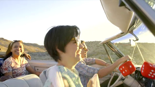 朋友们开着红色的敞篷车穿过沙漠，女孩举着披肩迎着风视频素材