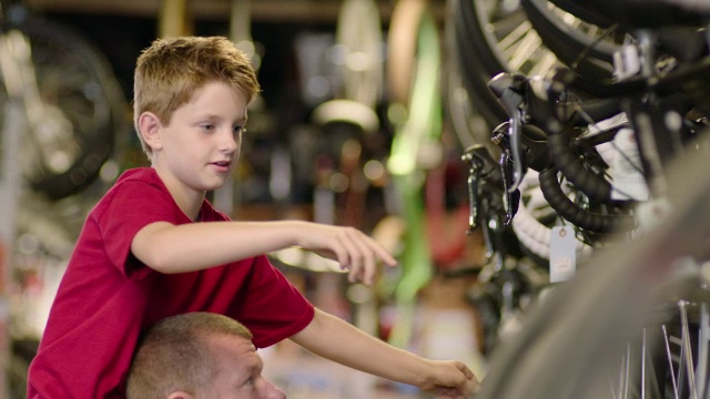 男孩骑在爸爸的肩膀上，指着自行车店里的一辆自行车视频下载