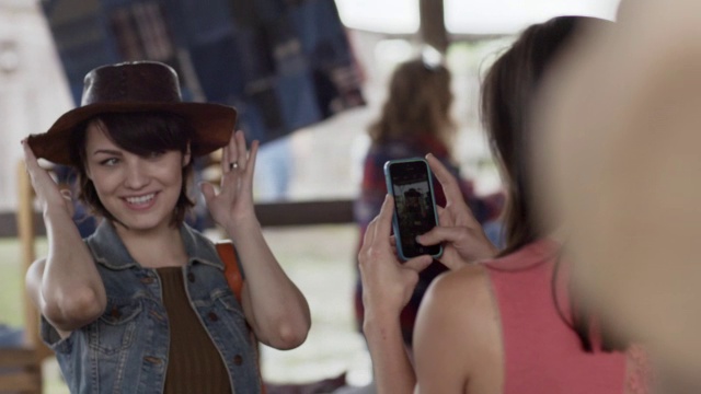 一个年轻女子在西部商店里拍了朋友试牛仔帽的有趣照片视频素材