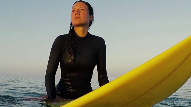美丽的女性冲浪者坐在冲浪板在日出在冲浪休息和海浪在大西洋海岸在法国南部海岸。视频下载