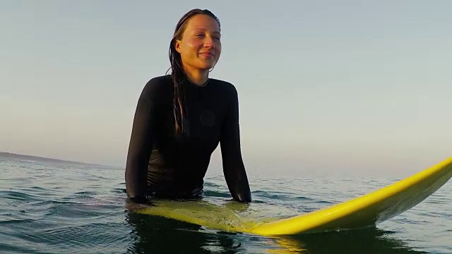 美丽的肖像，微笑的女性冲浪者坐在冲浪板在日出在冲浪休息和海浪在大西洋海岸在法国南部海岸。视频下载
