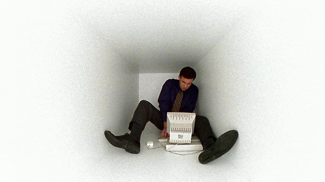 宽镜头的人坐在狭窄的白色盒子里使用电脑/从右向左滑动视频下载