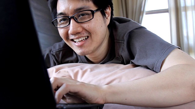 快乐的人戴着眼镜使用笔记本电脑在床上进行在线聊天，交流，或娱乐目的视频素材