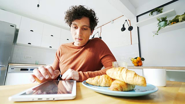 年轻人一边吃早餐一边用平板电脑。视频素材