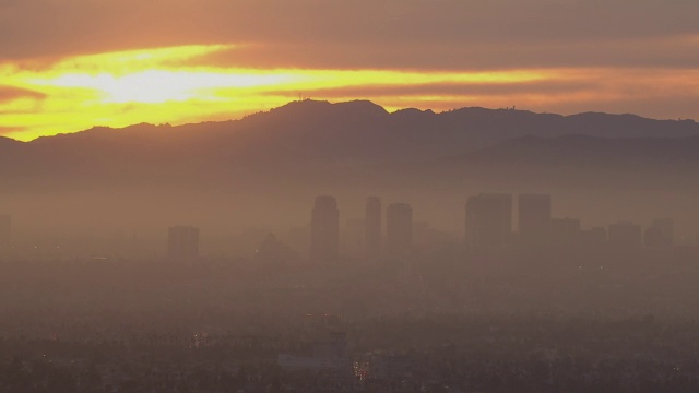 日落在圣塔莫尼卡山脉上空创造了明亮的色彩，而洛杉矶的摩天大楼被烟雾包围。视频素材