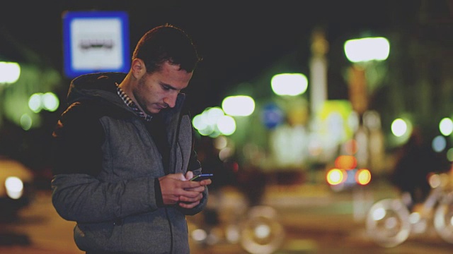 年轻男子晚上在城市里使用智能手机视频素材