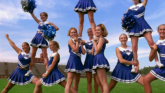 低角度广角镜头穿着制服的年轻女啦啦队员在球场上为四人金字塔欢呼视频下载