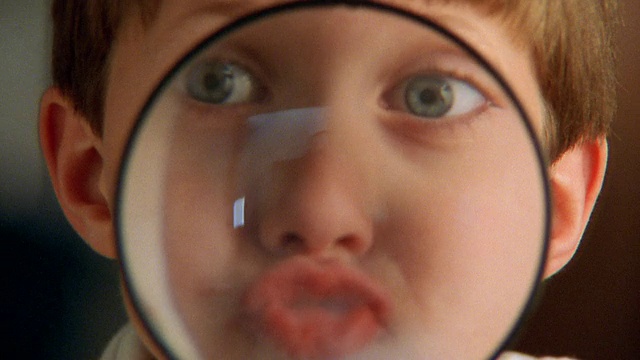 近距离看，小男孩透过放大镜做鬼脸视频素材