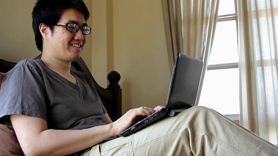 戴眼镜的快乐男人在床上用笔记本电脑在线聊天或视频会议视频素材