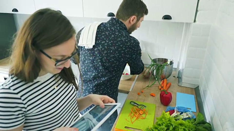 一对年轻夫妇用平板电脑一起做饭。视频素材