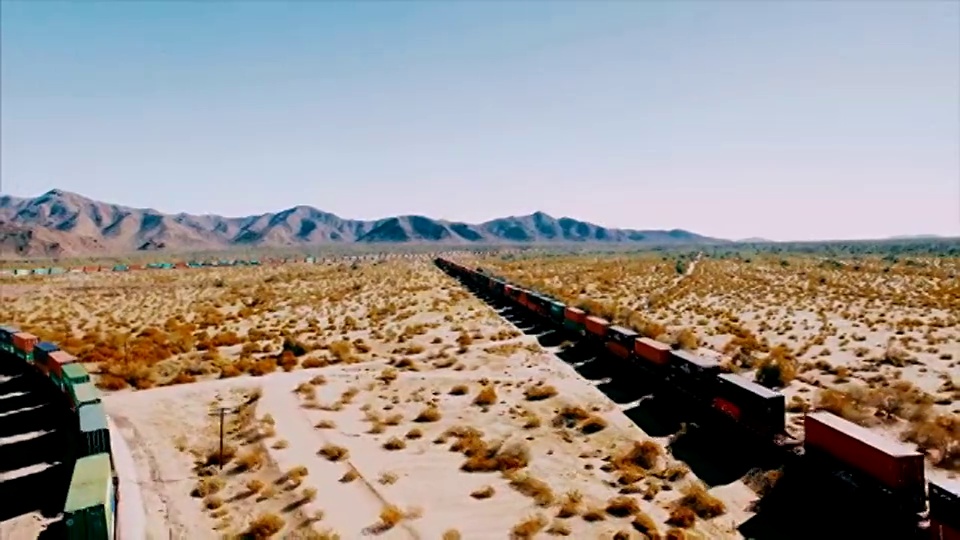 无人机从左到右跟踪一列集装箱货运列车，这列火车在干旱的美国沙漠的铁路上飞驰而下。视频下载