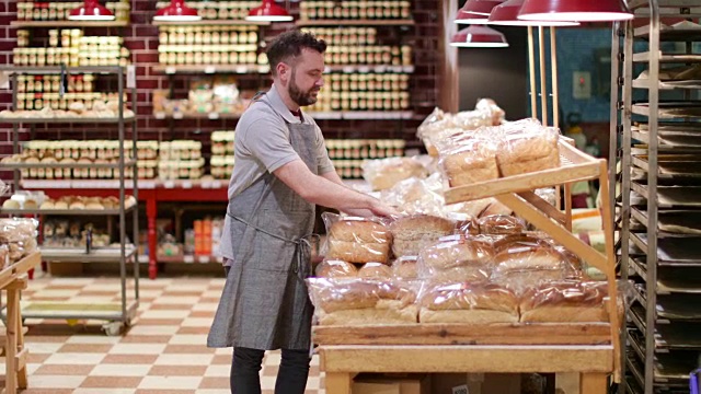 面包师在面包店的货架上，看着相机视频下载